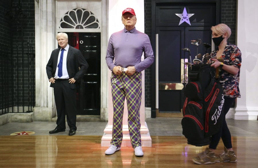 A member of the Madame Tussauds studios team places a set of golf clubs next to a wax figure of US President Donald Trump which has been re-dressed in golf wear following the 2020 US presidential election, in London, Wednesday, Nov. 4, 2020.  Joe Biden was elected Saturday, Nov. 7, 2020 as the 46th president of the United States, defeating President Donald Trump in an election that played out against the backdrop of a pandemic, its economic fallout and a national reckoning on racism.