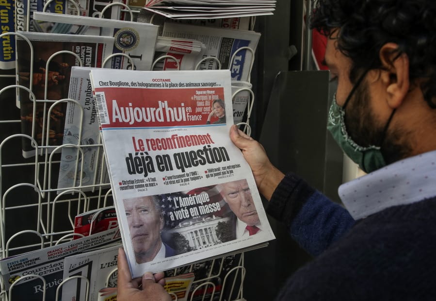 A man wearing a face mask as a precaution against the coronavirus reads the headlines about the U.S. presidential elections at a newspapers stand in Paris, Wednesday, Nov. 4, 2020. The world is watching as millions of Americans cast their ballots for the next president on Tuesday.