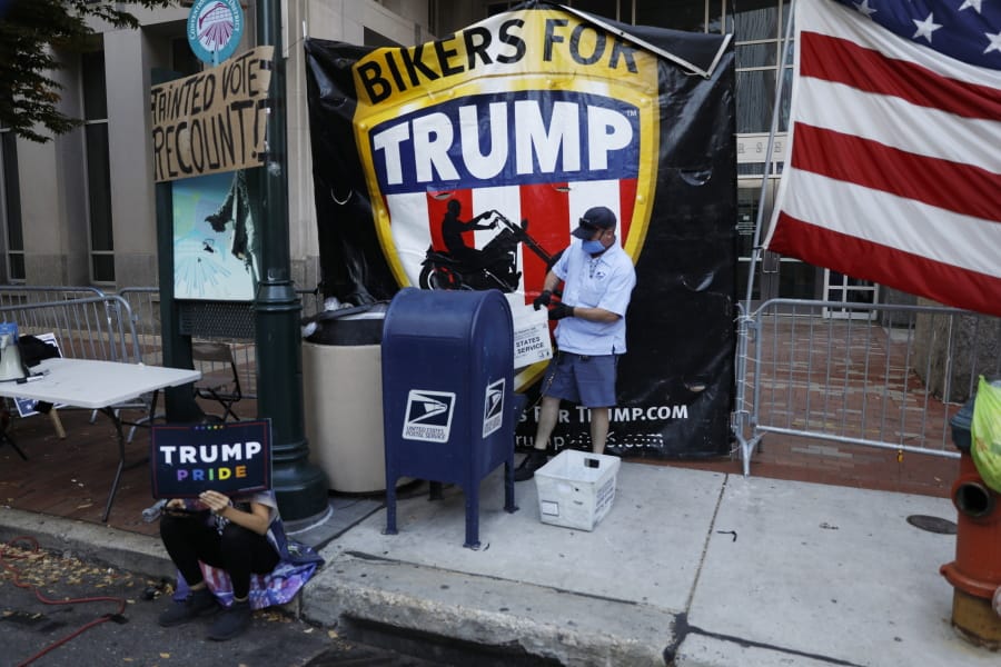A postal worker collects mail from a mailbox inside the protest pen, as a handful of supporters of President Donald Trump continue to demonstrate, outside the Pennsylvania Convention Center in Philadelphia, Tuesday, Nov. 10, 2020.