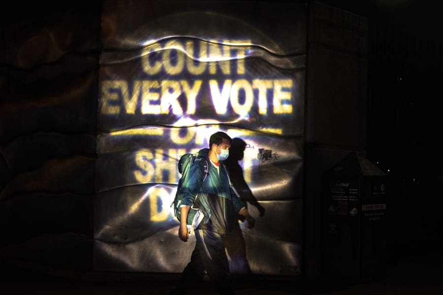 A man walks through a projected election slogan during protests following the Nov. 3 presidential election in Portland, Or. Wednesday, Nov. 4, 2020.