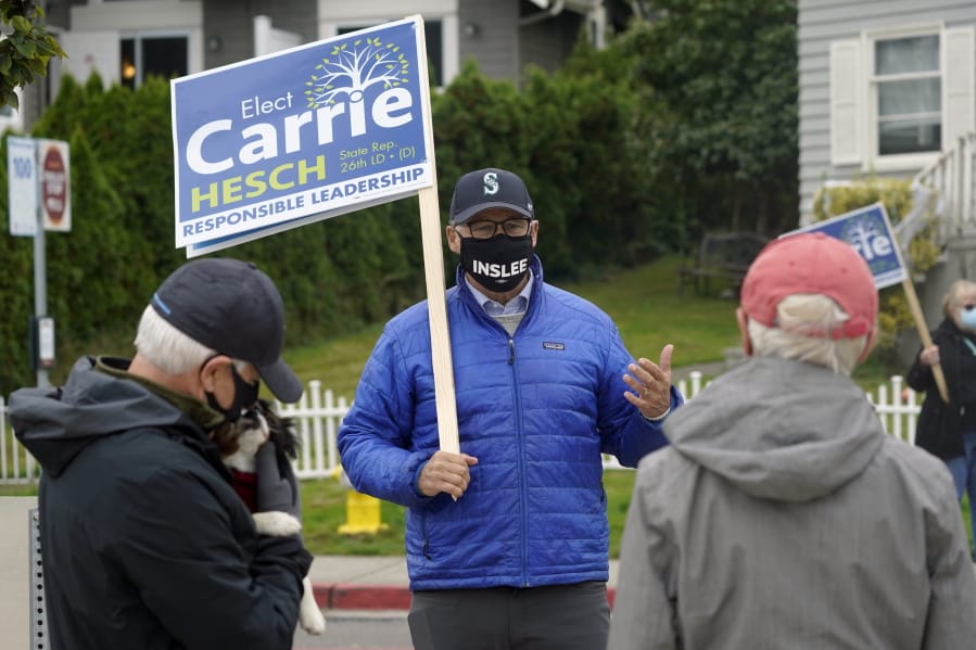 Washington Gov. Jay Inslee, center, talks with pedestrians, Wednesday, Oct. 28, 2020, in Gig Harbor, Wash., during a sign-waving event for Carrie Hesch, right, a Democrat who is running against Rep. Jesse Young, R-Gig Harbor, in the upcoming election. Inslee is being challenged by Republican Loren Culp, who is currently Chief of Police in Republic, Wash. (AP Photo/Ted S.