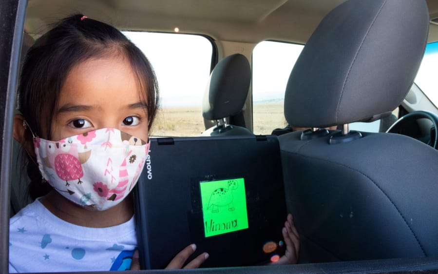 Second-grader Winona Begaye uploads homework in her family&#039;s vehicle in a dirt lot near Blue Gap, Ariz., on Sept. 25, 2020. Navajo Nation schools have remained virtual this fall because it&#039;s too dangerous to reopen their doors. To help families with no internet or poor access get online, the Pinon Unified School District outfitted school buses with Wi-Fi.