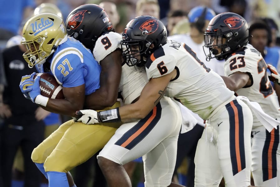 FILE - In this Oct. 5, 2019, file photo, UCLA running back Joshua Kelley, left, is tackled by Oregon State linebackers Hamilcar Rashed Jr. (9) and John McCartan (6) during the first half of an NCAA college football game in Pasadena, Calif. While the offense is still coming together with presumed starting quarterback Tristan Gebbia, it&#039;s Oregon State&#039;s defense that should worry opponents.