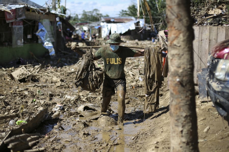 A policeman carries his belongings across debris and muds at the typhoon-damaged Kasiglahan village in Rodriguez, Rizal province, Philippines on Friday, Nov. 13, 2020. Thick mud and debris coated many villages around the Philippine capital Friday after Typhoon Vamco caused extensive flooding that sent residents fleeing to their roofs and killing dozens of people.