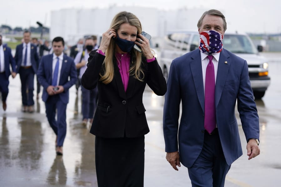 FILE- In this July 15, 2020, file photo Sen. Kelly Loeffler, R-Ga., puts on a face mask as she walks with Sen. David Perdue, R-Ga., right, at UPS Hapeville Airport Hub in Atlanta.
