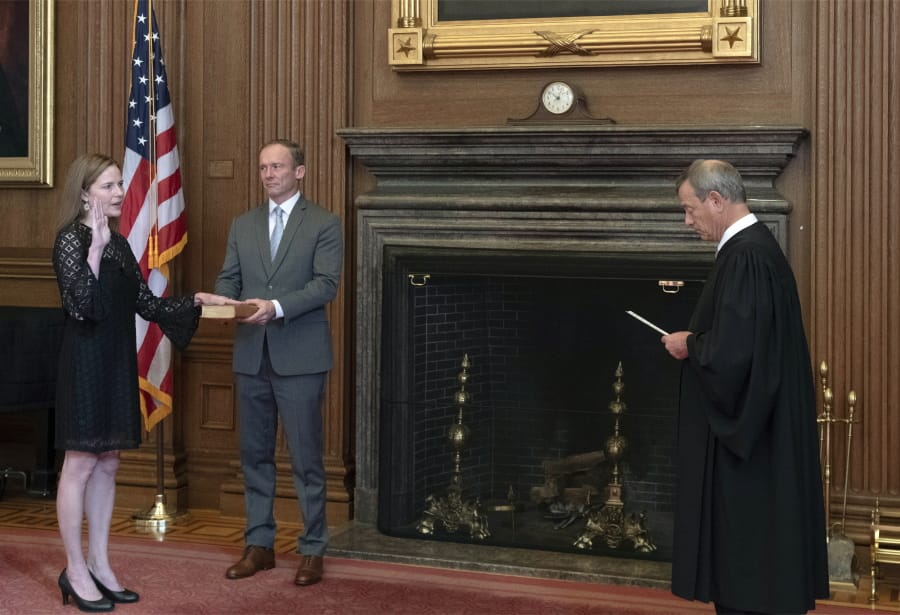 In this image provided by the Collection of the Supreme Court of the United States, Chief Justice John G. Roberts, Jr., right, administers the Judicial Oath to Judge Amy Coney Barrett in the East Conference Room of the Supreme Court Building, Tuesday, Oct. 27, 2020, in Washington as Judge Barrett&#039;s husband, Jesse M. Barrett, holds the Bible.