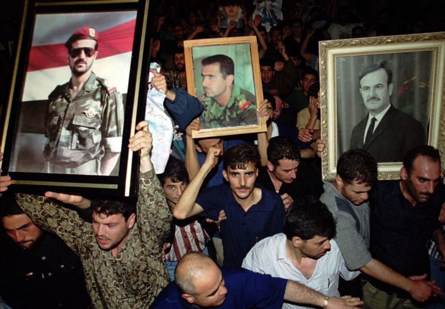 FILE - In this June 10, 2000 file photo, Syrian mourners wave portraits of President Hafez Assad, right, and his two sons Bashar, center, and Basil who died in a car accident in 1994 to mourn the death of their president, in Damascus, Syria. For fifty years, the Assad family has controlled Syria, overseeing transformations, modernization, uprisings and upheaval while becoming among the most divisive figures of their time.