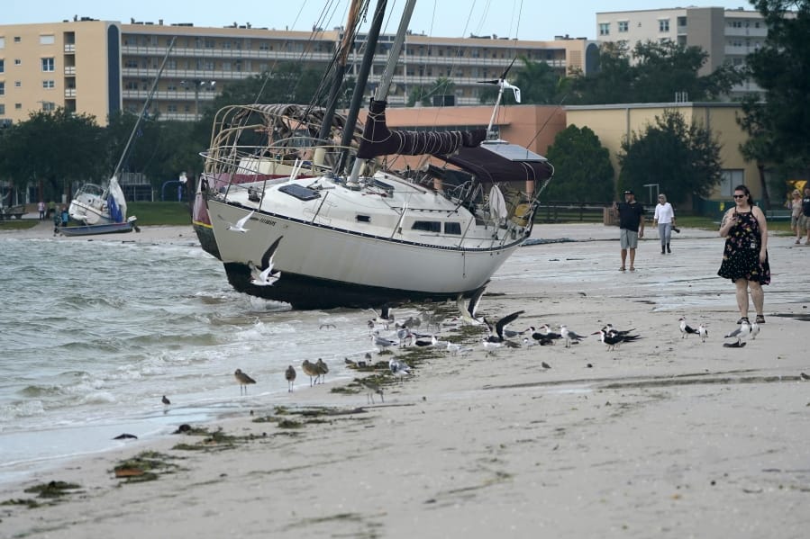 People walk past boats on the beach in the aftermath of Tropical Storm Eta, Thursday, Nov. 12, 2020, in Gulfport, Fla. Eta dumped torrents of blustery rain on Florida&#039;s west coast as it slogged over the state before making landfall near Cedar Key, Fla.