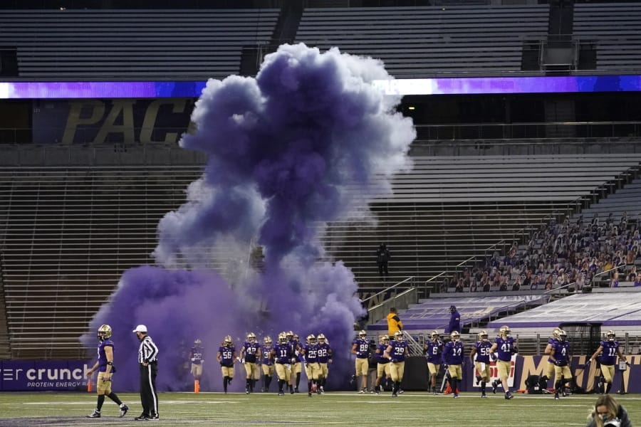 Washington players run out of a tunnel through a cloud of purple smoke in front of empty seats at Husky Stadium before an NCAA college football game against Utah, Saturday, Nov. 28, 2020, in Seattle. Due to the COVID-19 pandemic, no fans were in attendance at the game. (AP Photo/Ted S.