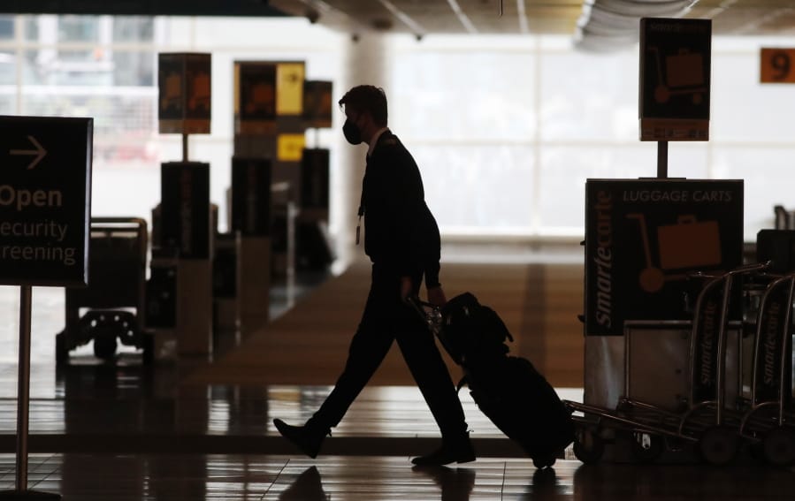 FILE - In this Thursday, April 9, 2020, file photo, a lone airline crew member pulls his bags behind him as he walks through the baggage-claim area at Denver International Airport in Denver, amid the coronavirus outbreak.