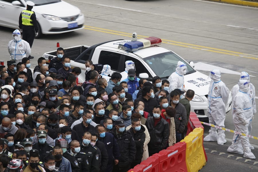 Security workers in protective suits stand by as workers wearing face masks to help curb the spread of the coronavirus gather for COVID-19 testing at the Shanghai Pudong International Airport in Shanghai, Monday, Nov. 23, 2020. Chinese authorities are testing millions of people, imposing lockdowns and shutting down schools after multiple locally transmitted coronavirus cases were discovered in three cities across the country last week.