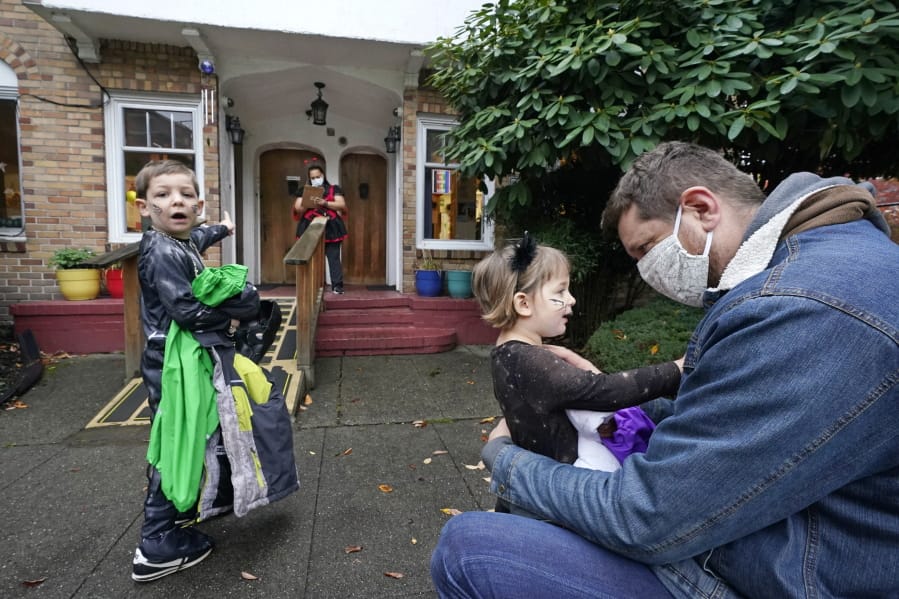 Alex Stonehill gets a goodbye from his daughter Helenore, 2, as her brother Malcolm, 4, motions to a friend arriving at the Community Day Center for Children on Thursday, Oct. 29, 2020, in Seattle. As more families make the jump back to group day care this fall in an attempt to restart lives and careers, many parents, pediatricians and care operators are finding that new, pandemic-driven rules offer a much-needed layer of safety but also seem incompatible with the germy reality of childhood.