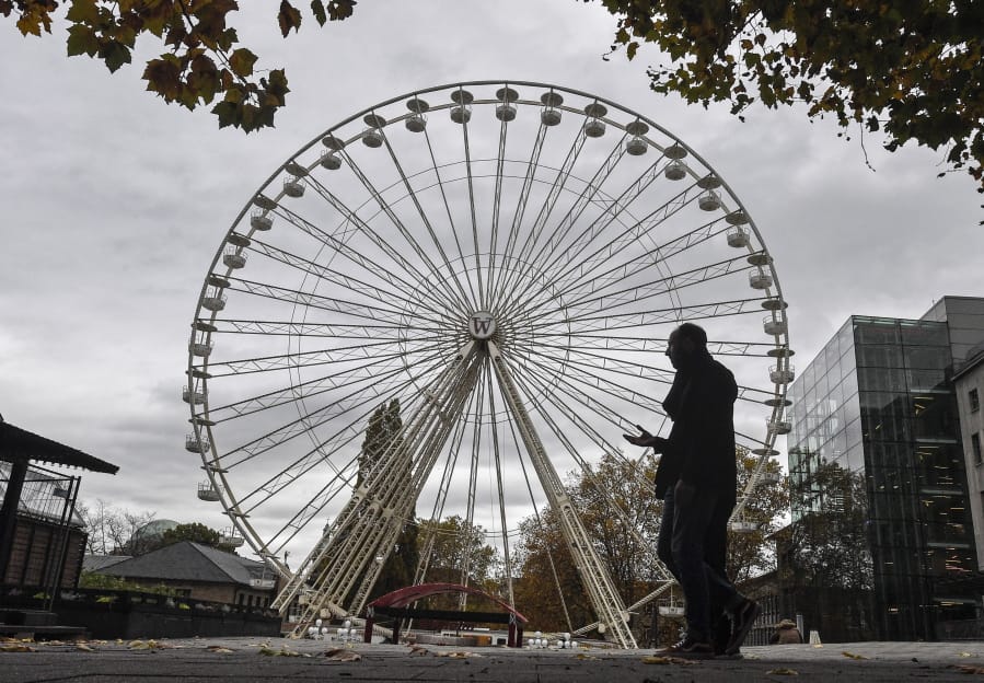 A man passes a closed Ferris wheel in the city center of Essen, Germany, Monday, Nov. 2, 2020. A one month long partial lockdown due to the coronavirus pandemic becomes effective in Germany on Monday.