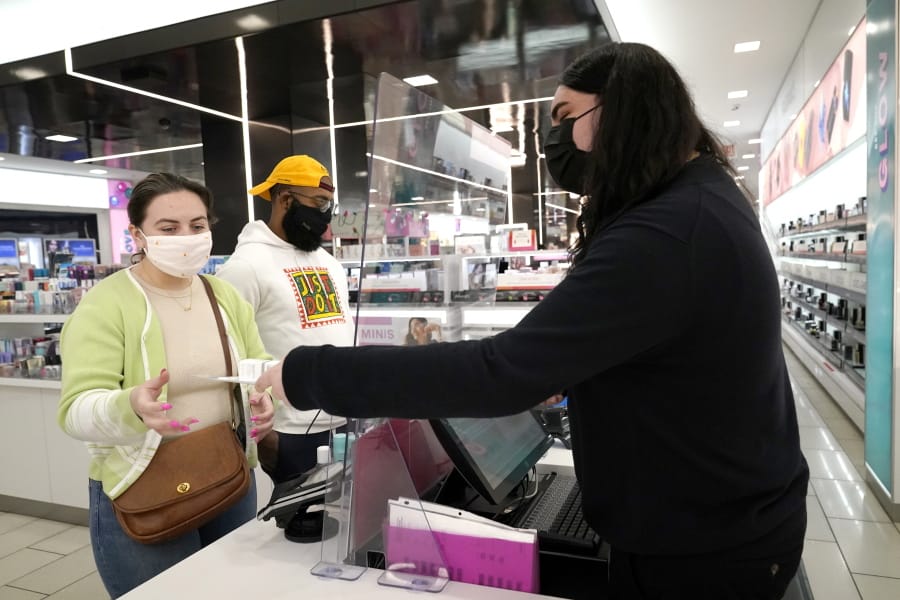 Cashier Druhan Parker, right, works behind a plexiglass shield Thursday, Nov. 19, 2020, as he checks out shoppers Cassie Howard, left, and Paris Black at an in Chicago. The accelerating surge of coronavirus cases across the U.S. is causing an existential crisis for America&#039;s retailers and spooking their customers just as the critically important holiday shopping season nears.