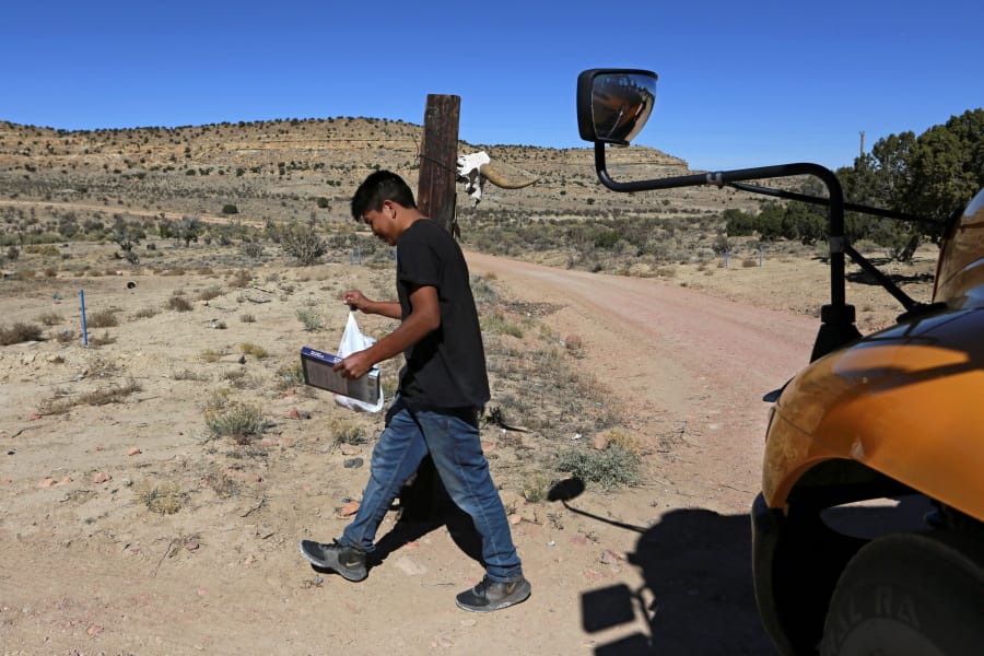 A student carries a math book delivered by school bus driver Kelly Maestas along his rural route outside Cuba, N.M., Oct. 19, 2020. The switch to remote learning in rural New Mexico has left some students profoundly isolated -- cut off from others and the grid by sheer distance. The school system is sending school buses to students&#039; far-flung homes to bring them assignments, meals and a little human contact.