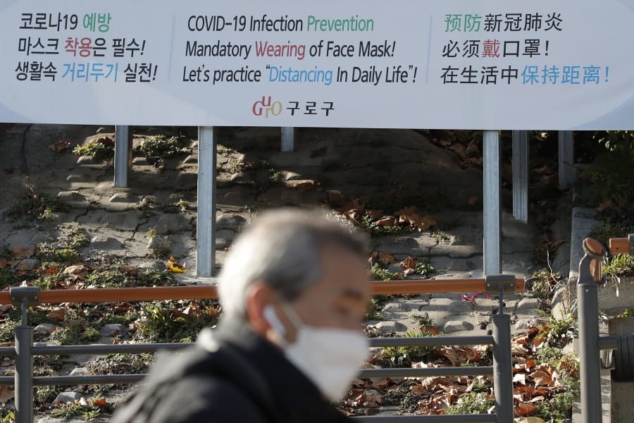 A man wearing a face mask walks past a banner showing precautions against the coronavirus in Seoul, South Korea, Monday, Nov. 23, 2020.