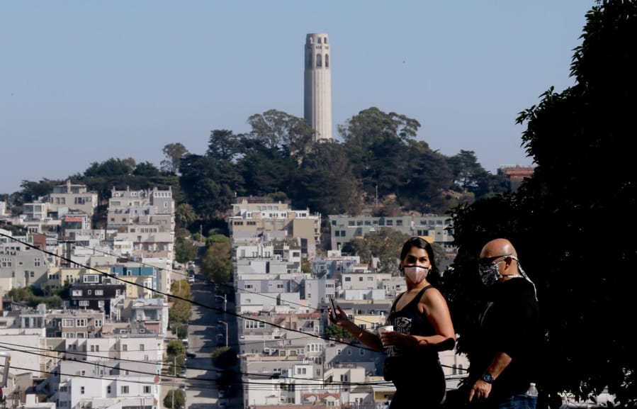 Coit Tower serves as a backdrop for people walking along Leavenworth Street in San Francisco on Friday, Aug. 23, 2020.