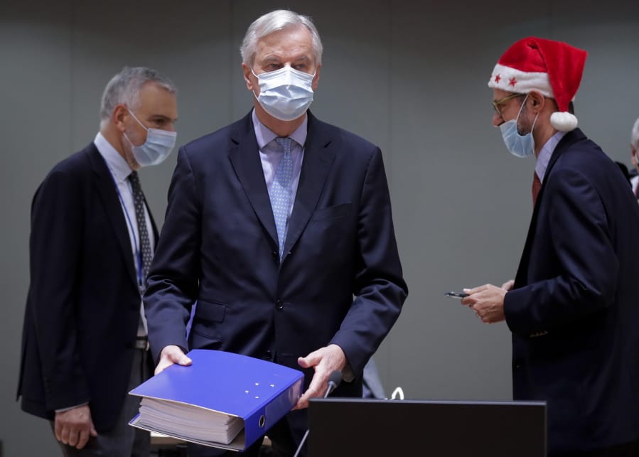 A colleague wears a Christmas hat as European Union chief negotiator Michel Barnier, center, carries a binder of the Brexit trade deal during a special meeting of Coreper, at the European Council building in Brussels, Friday, Dec. 25, 2020. European Union ambassadors convened on Christmas Day to start an assessment of the massive free-trade deal the EU struck with Britain. After the deal was announced on Thursday, EU nations already showed support for the outcome and it was expected that they would unanimously back the agreement, a prerequisite for its legal approval.
