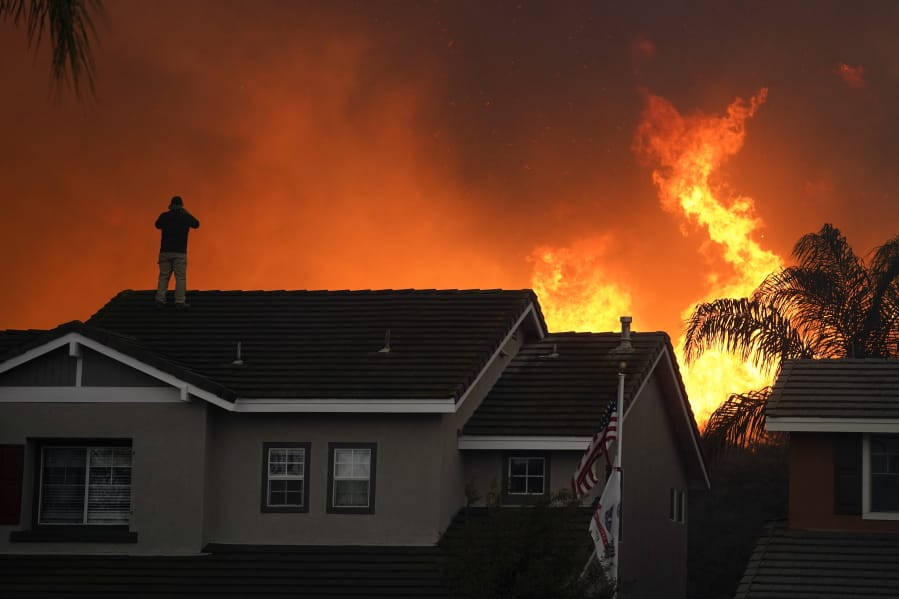 FILE - In this Tuesday, Oct. 27, 2020 file photo, Herman Termeer, 54, stands on the roof of his home as the Blue Ridge Fire burns along the hillside in Chino Hills, Calif. An overheating world obliterated weather records in 2020 -- an extreme year for hurricanes, wildfires, heat waves, floods, droughts and ice melt -- the United Nations&#039; weather agency reported Wednesday, Dec. 2, 2020. (AP Photo/Jae C.