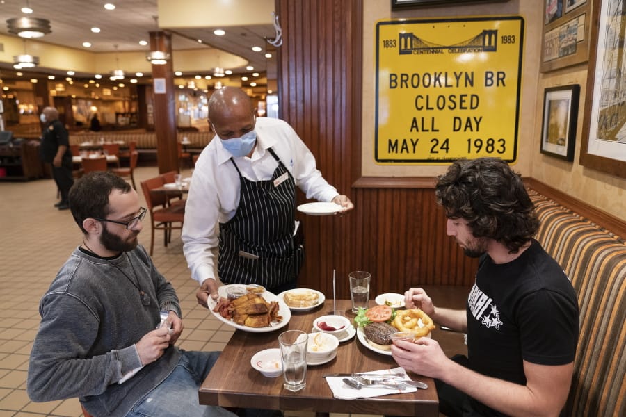 FILE- In this Sept. 30, 2020 file photo, waiter Lenworth Thompson serves lunch to David Zennario, left, and Alex Ecklin at Junior&#039;s Restaurant in New York.  The U.S. services sector, where most Americans work, registered its fifth consecutive month of expansion in October 2020.