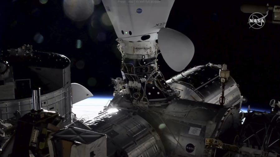 In this image taken from NASA TV the Dragon cargo capsule docks at the International Space Station, Monday, Dec. 7, 2020, alongside a Dragon crew capsule that carried up astronauts three weeks ago.