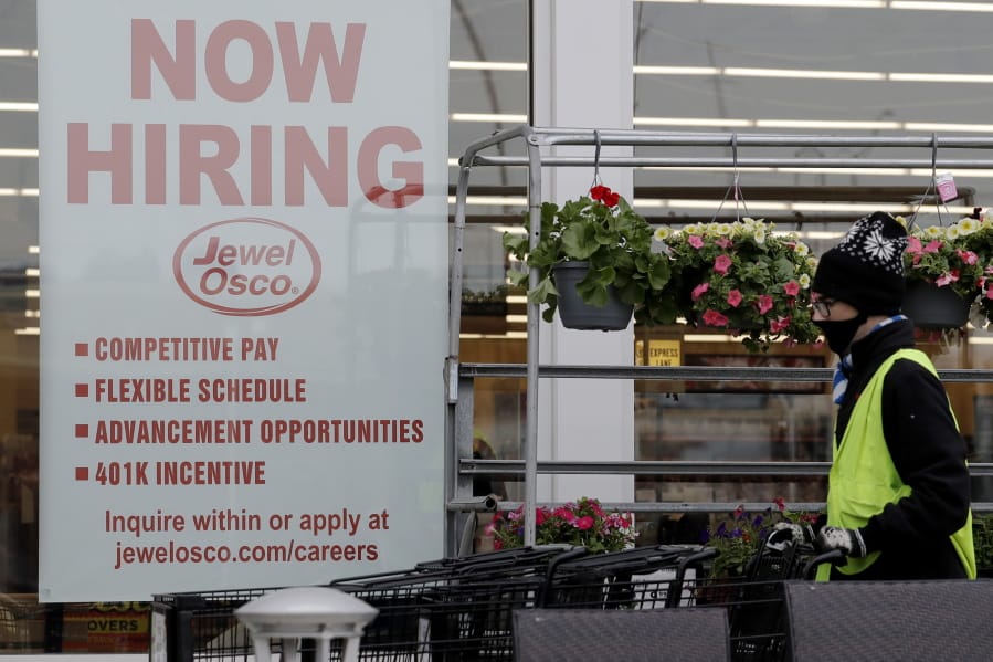 A man pushes carts as a hiring sign shows at a Jewel Osco grocery store in Deerfield, Ill., Thursday, April 23, 2020. Friday, Dec. 4,  monthly U.S. jobs report will help answer a key question hanging over the economy: Just how much damage is being caused by the resurgent coronavirus, the resulting restrictions on businesses and the reluctance of consumers to shop, travel and dine out? (AP Photo/Nam Y.