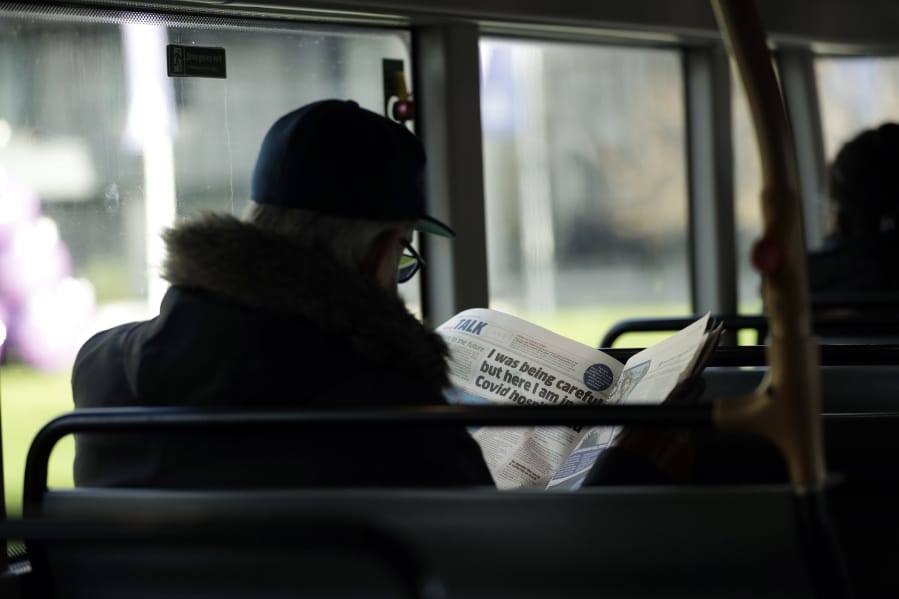 A man reads a newspaper with an article about COVID-19 as he sits on a bus during England&#039;s second coronavirus lockdown in London, Tuesday, Dec. 1, 2020. England&#039;s second coronavirus lockdown is due to end tomorrow to be replaced by a three-tier system.