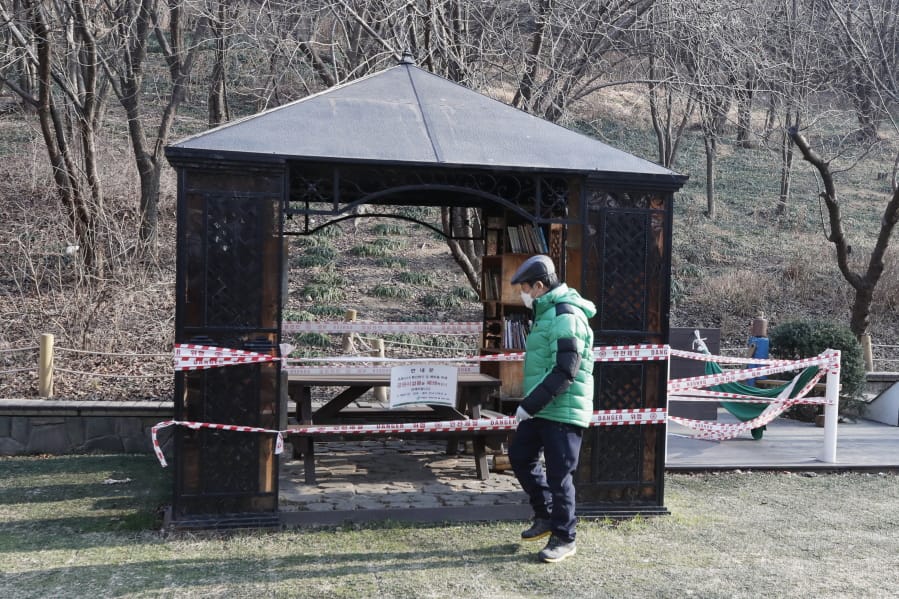 FILE - In this Tuesday, Dec. 22, 2020 file photo a man wearing a face mask walks past a rest area taped for social distancing and a precaution against the coronavirus in Seoul, South Korea.