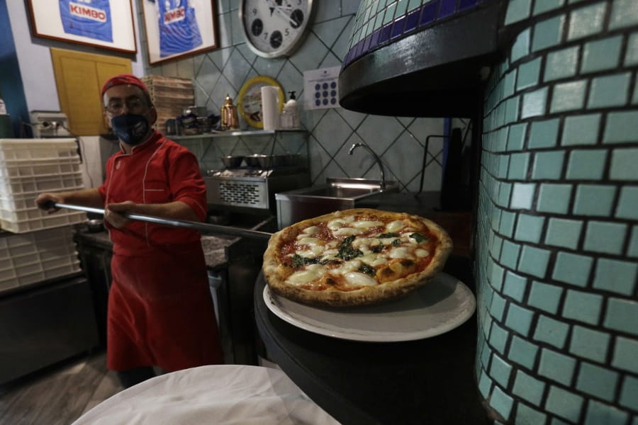 Eugenio Iorio wears a face mask to curb the spread of COVID-19 as he bakes a pizza at a restaurant in Naples, Italy.