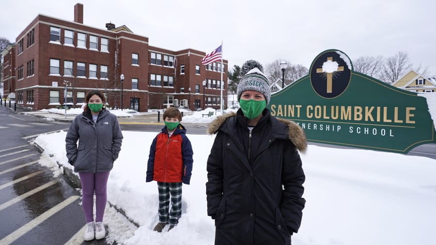 Head of School Jennifer Kowieski, right, poses with students Madeline Perry, of Brookline, Mass., left, and Landon Freytag, of Newton, Mass., center, outside the Saint Columbkille Partnership School, a Catholic school, Friday, Dec. 18, 2020, in the Brighton neighborhood of Boston. The families of both students decided to switch to the school, avoiding the challenges of remote learning at many public schools.