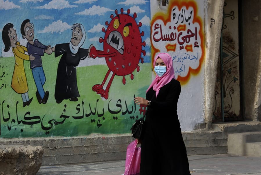 A woman walks past a mural encouraging the wearing of face masks amid the coronavirus pandemic, on the main road of Nusseirat refugee camp, central Gaza Strip, on Nov. 24, 2020. Arabic reads: &quot;protect yourself, together we protect the old.&quot; The prickly orb is on every news and medical site. It&#039;s all over TV and on flyers for COVID car cleaning.