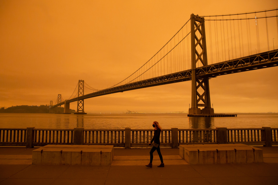 A woman walks along The Embarcadero under an orange smoke-filled sky in San Francisco, California on September 9, 2020. More than 300,000 acres are burning across the northwestern state including 35 major wildfires, with at least five towns &quot;substantially destroyed&quot; and mass evacuations taking place.