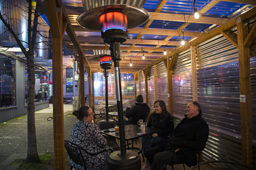 Heaters at the outdoor dining area of the Main Event in downtown Vancouver add warmth for customers Alyson Hilken, from left, Krissy Sadewasser and John Laughlin as they enjoy a happy hour drink.  At top, a sign informs customers of alternative dining options at Main Event.
