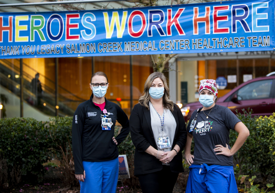 Melissa Glascock, from left, a respiratory therapist, Colette Reilly, a nurse manager, and Lisa Streissguth-Kasberg, a charge nurse, pose in front of a "Heroes Work Here" banner outside Legacy Salmon Creek Medical Center. Clark County hospitals have seen spikes in coronavirus patients this fall and winter.