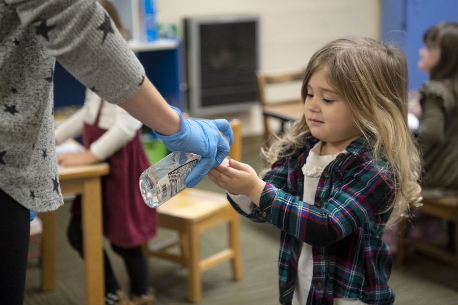 Parent helper Sarah Stowe gives Aurora Lund, 3, a pump of hand sanitizer following snack time on Tuesday at the Camas-Washougal Parent Co-Op preschool. All students received hand sanitizer after snack time before returning to coloring projects.