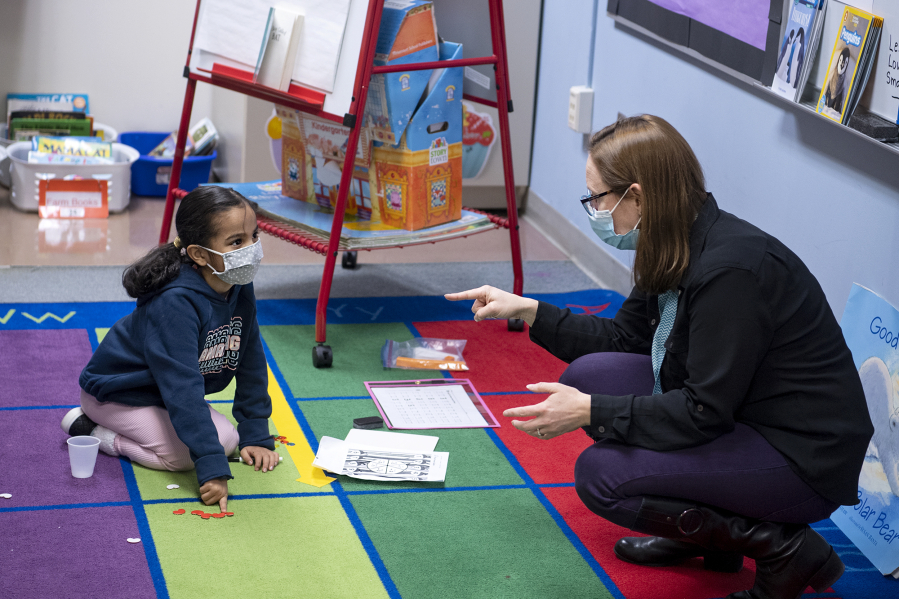 Kindergartner Camila Huesos-Delgado works on a math assignment while teacher Jessica Roth helps at Captain Strong Primary School in Battle Ground.