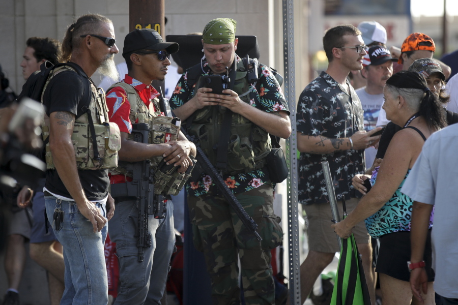 FILE - In this June 20, 2020 file photo, gun-carrying men wearing Hawaiian print shirts associated with the boogaloo movement watch a demonstration near where President Trump had a campaign rally in Tulsa, Okla. People following the anti-government boogaloo movement, which promotes violence and a second U.S. civil war, have been showing up at protests across the nation armed and wearing tactical gear. But the movement has also adopted an unlikely public and online symbol: Hawaiian print shirts.