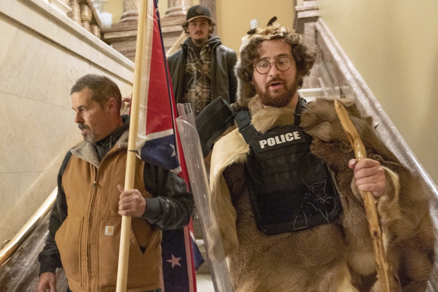 FILE - In this Jan. 6, 2021 file photo, insurrectionists loyal to President Donald Trump, including Aaron Mostofsky, right, and Kevin Seefried, left, walk down the stairs outside the Senate Chamber in the U.S. Capitol, in Washington.  More than 125 people have been arrested so far on charges related to the violent insurrection at the U.S. Capitol, where a Capitol police officer and four others were killed.
