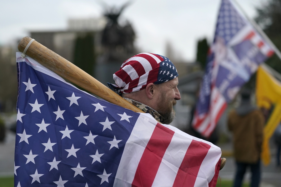 A man carries a U.S. flag attached to a baseball bat as he waits at the Capitol in Olympia, Wash., Wednesday, Jan. 6, 2021, before the start of a protest rally against the counting of electoral votes in Washington, DC, affirming President-elect Joe Biden&#039;s victory. People supporting President Donald Trump and other supporters began arriving at the Capitol mid-morning for a protest rally Wednesday that was expected to begin at noon. (AP Photo/Ted S.
