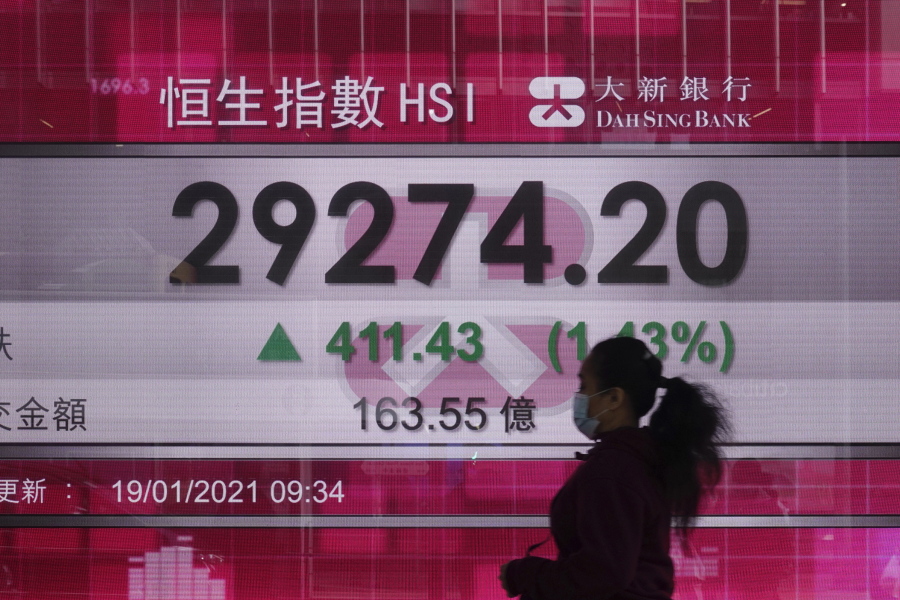 A woman walks past a bank&#039;s electronic board showing the Hong Kong share index at Hong Kong Stock Exchange in Hong Kong Tuesday, Jan. 19, 2021. Shares advanced in Asia on Tuesday as the changing of the guard in the U.S. raised hopes for more support for the economy and more aggressive measures to fight the pandemic.