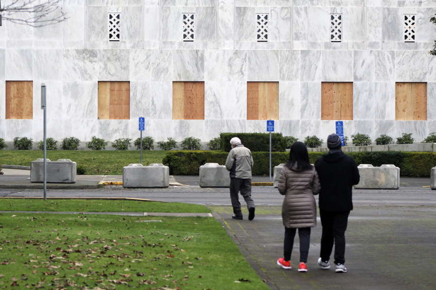 A couple stops to look at the Oregon State Capitol, whose first-floor windows have been boarded up Friday in Salem, Ore. Large cement blocks have also been placed in front of the building, which has been closed to the public since March because of the coronavirus pandemic.
