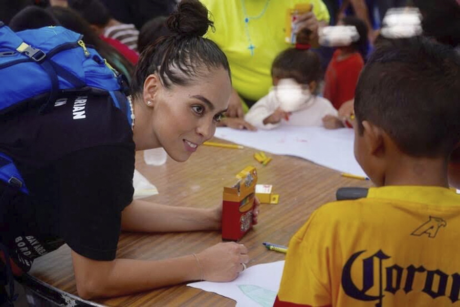 In this October 2019 photo provided by Pocho Sanchez, Daniela Dominguez, assistant professor in counseling psychology at University of San Francisco, draws and chats with children from Honduras at a migrant camp in Matamoros, Mexico. Dominguez said mutual aid networks are part of the Latino culture where people may feel safer getting help from their own community rather than government entities or formal charities.