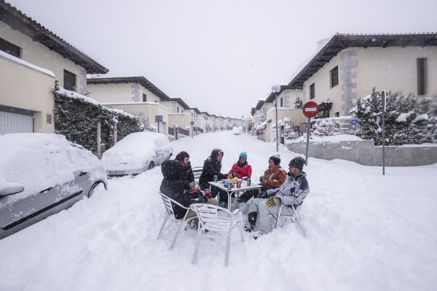 Neighbours have drinks in the middle of the street during a heavy snowfall in Bustarviejo, outskirts of Madrid, Spain, Saturday, Jan. 9, 2021. A persistent blizzard has blanketed large parts of Spain with 50-year record levels of snow, halting traffic and leaving thousands trapped in cars or in train stations and airports that suspended all services as the snow kept falling on Saturday. Half of Spain is on alert, with five provinces on their highest level of warning.