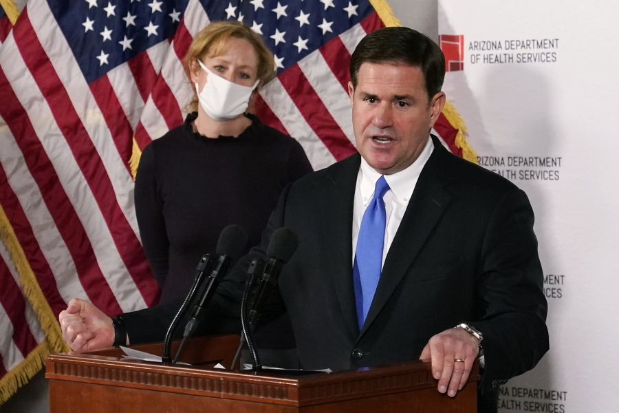 FILE - In this Dec. 2, 2020, file photo, Arizona Gov. Doug Ducey answers a question about the arrival of a COVID-19 vaccine in Arizona, while Arizona Department of Health Services Director Dr. Cara Christ listens in Phoenix. As Arizona experienced periodic spikes in COVID-19 cases since last spring, Ducey frequently resisted calls to take strong measures. He has declined to institute a statewide mask mandate, allowed school districts to mostly make their own choices and allowed businesses to stay open. All of those choices by the Republican governor are now getting renewed scrutiny as the Grand Canyon state becomes what health officials call the latest &quot;hot spot of the world&quot; because of soaring case loads. (AP Photo/Ross D.