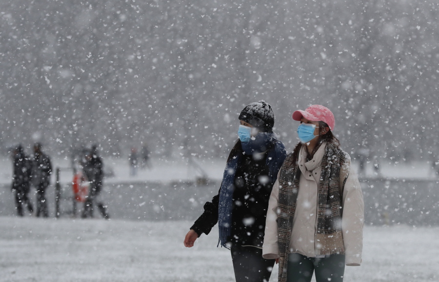 Pedestrians wearing face masks against the coronavirus pandemic walk in Kensington Gardens as snow falls in London, Sunday, Jan. 24, 2021.
