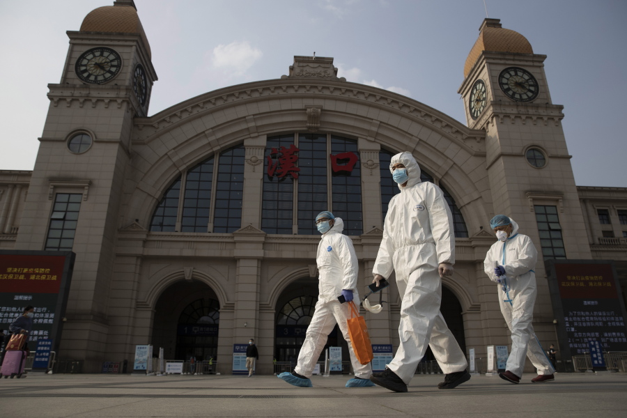 FILE - In this April 7, 2020, file photo, workers in protective suits walk past the Hankou railway station on the eve of its resuming outbound traffic in Wuhan in central China&#039;s Hubei province. China says a group of experts from the World Health Organization are due to arrive Thursday, Jan. 14, 2021, for an investigation into the origins of the coronavirus pandemic. A one-sentence announcement from the National Health Commission on Monday, Jan.