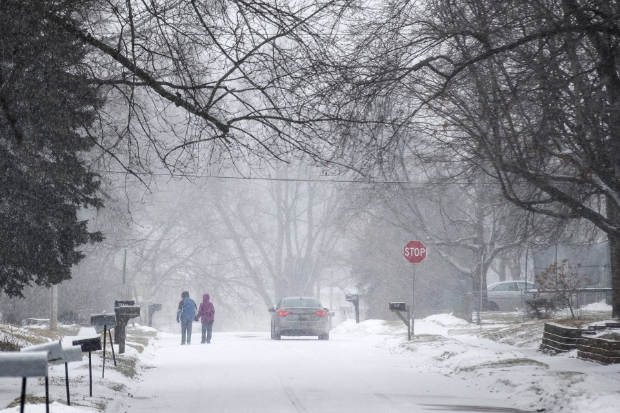 Two people hold hands while walking south on Madison Street toward 27th Avenue in Bellevue, Neb., during a winter storm warning on Monday, Jan. 25, 2021.