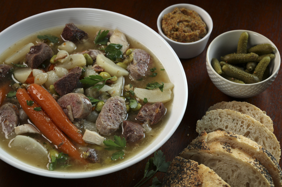 Pot au feu (boiled meats dinner) is served with accompaniments like carrots, pearl onions, fresh herbs, pickles, mustard.