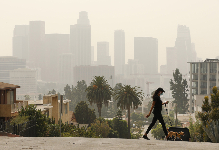 Breya Hodge walks her dog, Sophie, on Sept. 14 as smoke from the Bobcat Fire shrouds downtown Los Angeles.