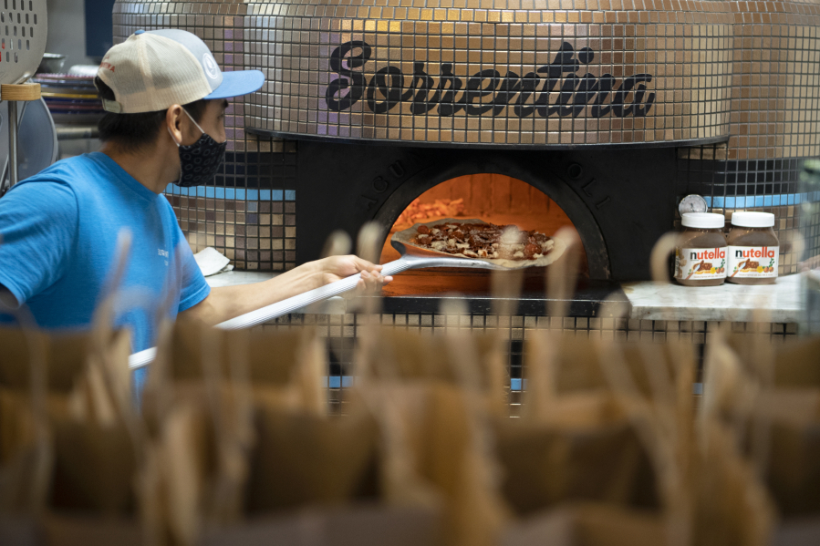 Antonio Fernandez pulls a pizza out of the wood-fired oven at Pizzeria La Sorrentina on Thursday. Support a Senior, Rescue a Restaurant started in January with a donation from Giving Group Realty in Vancouver to the nonprofit Northwest Wine &amp; Food Society, which in turn purchased gift cards from small local restaurants.